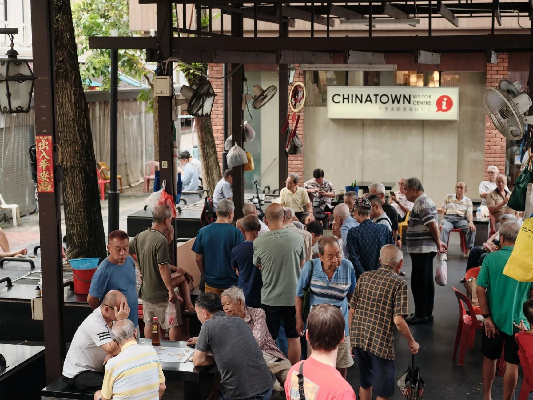 Community gathering at a Chinatown pavilion in Singapore with seniors playing chess and chatting