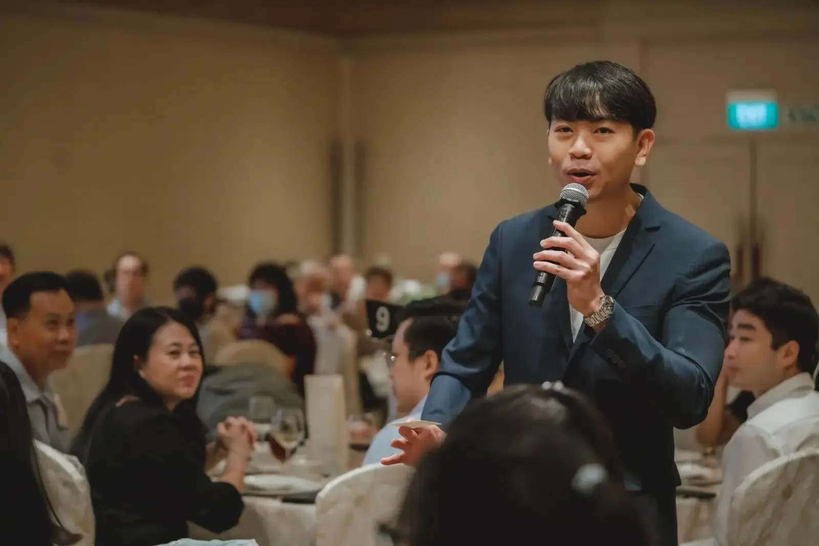 Emcee Rayson Soh mid-speech with microphone raised, engaging wedding guests at a Singapore ballroom
